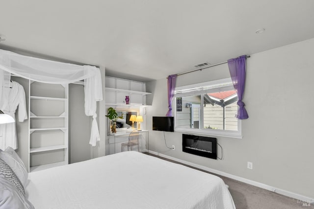 bedroom featuring visible vents, carpet flooring, baseboards, and a glass covered fireplace