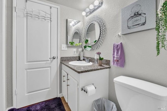 bathroom with toilet, vanity, and a textured wall