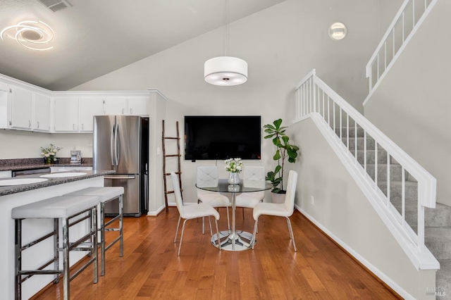 dining space featuring visible vents, baseboards, stairway, light wood-style floors, and high vaulted ceiling