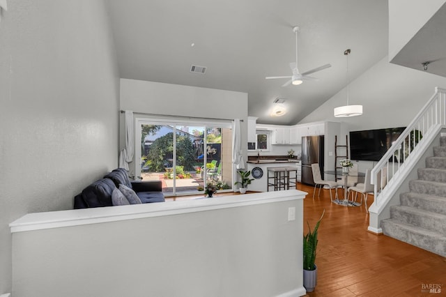 living area with stairway, wood finished floors, visible vents, high vaulted ceiling, and ceiling fan