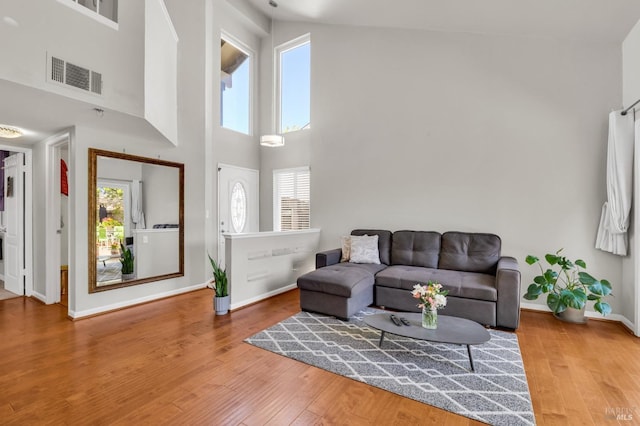 living area featuring wood finished floors, visible vents, a towering ceiling, and baseboards