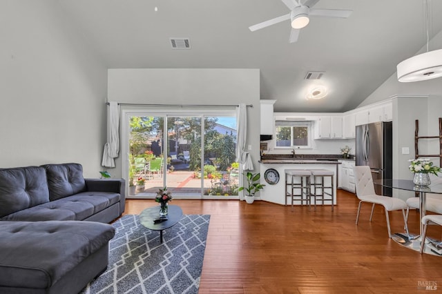 living area featuring ceiling fan, visible vents, wood finished floors, and vaulted ceiling