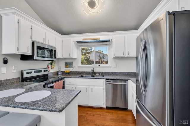 kitchen with wood finished floors, a peninsula, a sink, appliances with stainless steel finishes, and dark countertops