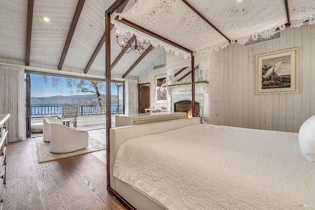 bedroom with lofted ceiling with beams, wood finished floors, access to outside, a lit fireplace, and wood walls