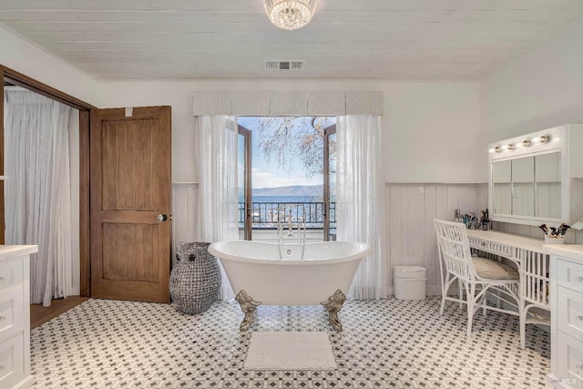 bathroom featuring visible vents, wainscoting, wooden ceiling, a soaking tub, and vanity