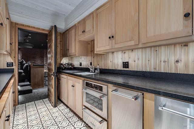 kitchen with light brown cabinets, dark countertops, a sink, and wooden walls