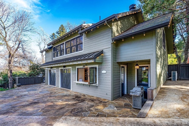 view of front of home with metal roof, a patio, an attached garage, fence, and driveway