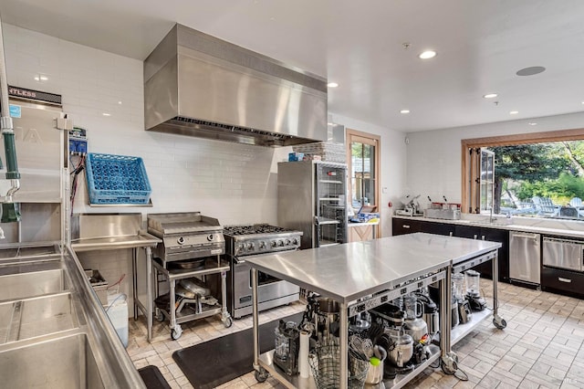 kitchen featuring tasteful backsplash, wall chimney exhaust hood, appliances with stainless steel finishes, stainless steel counters, and a wealth of natural light