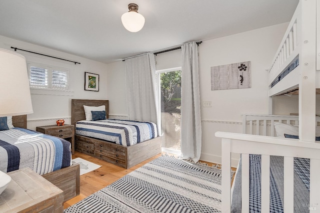 bedroom featuring light wood finished floors, multiple windows, and a wainscoted wall