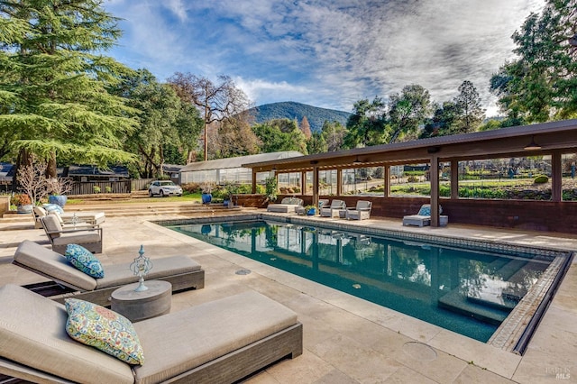 pool with an outdoor living space, a patio area, fence, and a mountain view