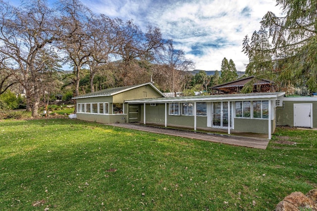 back of house featuring a sunroom, a lawn, and stucco siding