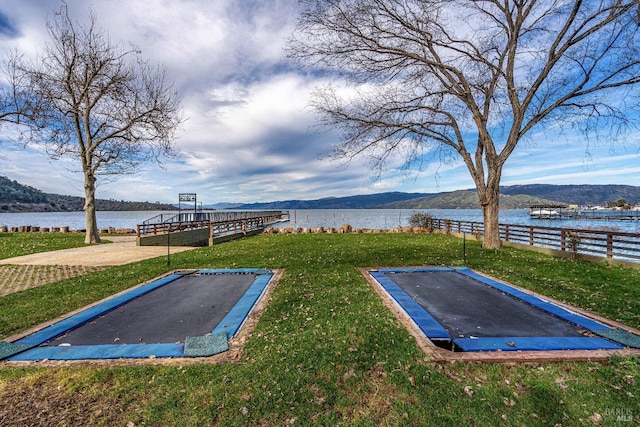 view of yard featuring a water view, a trampoline, and fence