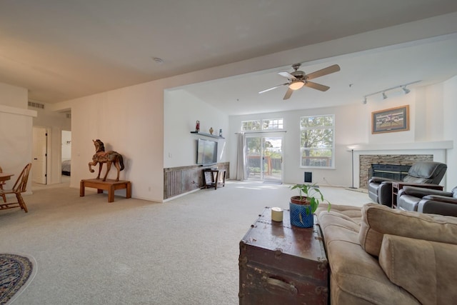 living room with ceiling fan, carpet floors, rail lighting, and a stone fireplace