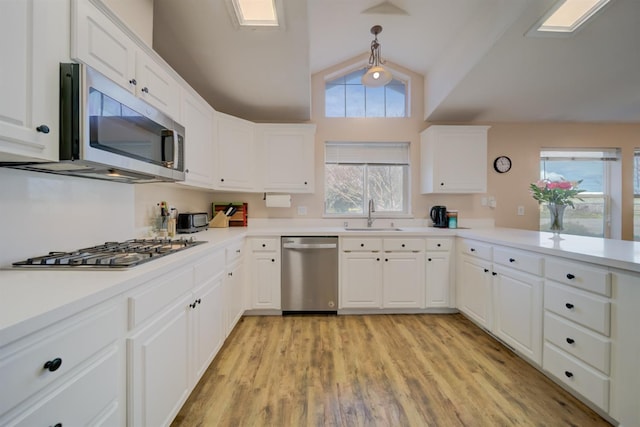 kitchen with appliances with stainless steel finishes, vaulted ceiling, white cabinets, and a sink