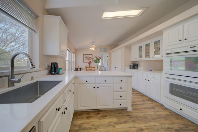 kitchen with light wood finished floors, white double oven, lofted ceiling, a peninsula, and a sink