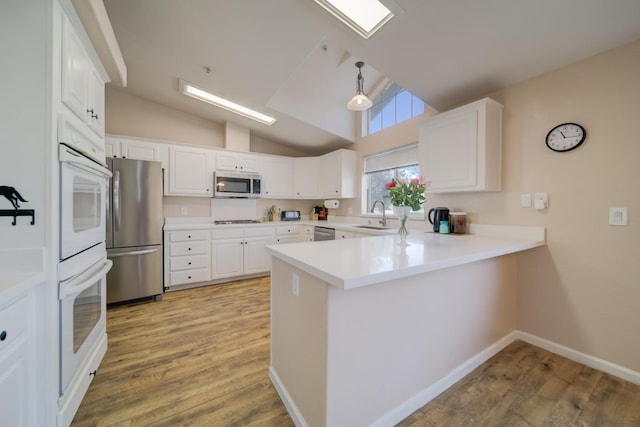 kitchen with stainless steel appliances, light wood-style floors, a sink, and a peninsula