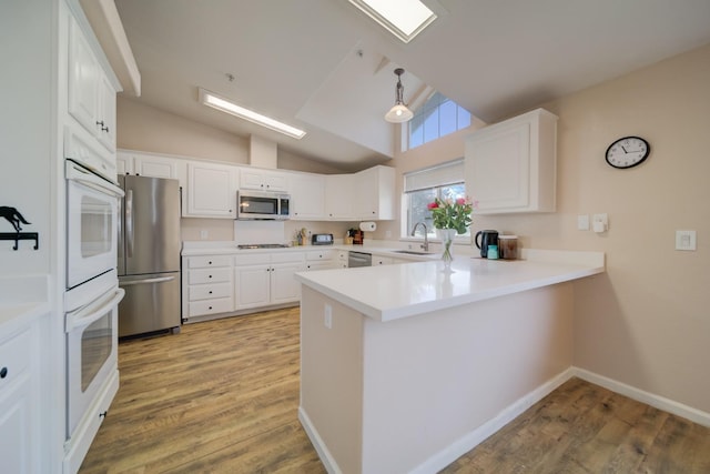 kitchen featuring a sink, light wood-style floors, stainless steel appliances, a peninsula, and lofted ceiling