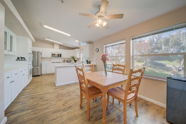 dining space with vaulted ceiling, light wood finished floors, a ceiling fan, and baseboards