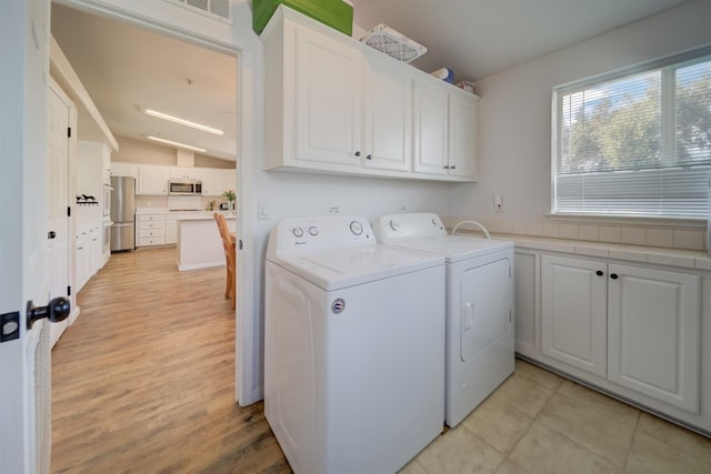 clothes washing area with washing machine and clothes dryer, light wood-style flooring, visible vents, and cabinet space