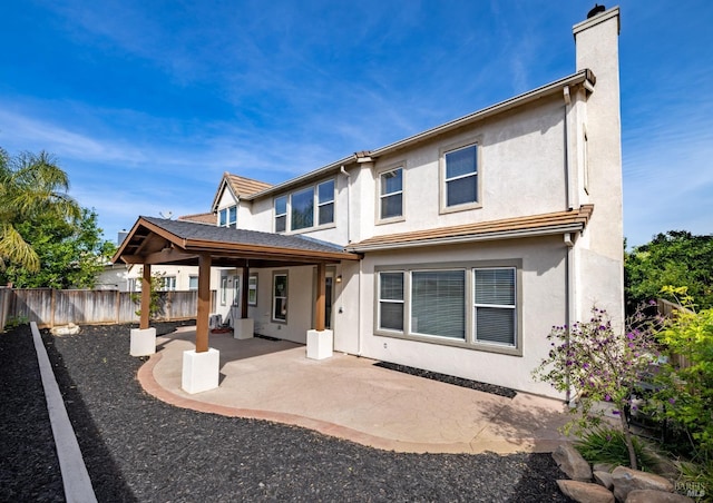 back of house with stucco siding, a chimney, fence, and a patio