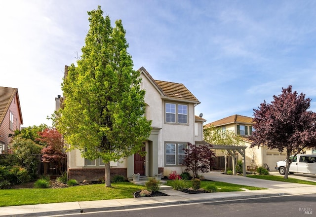 view of front of house featuring brick siding, fence, a front lawn, and stucco siding