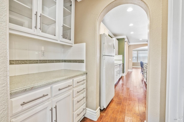 kitchen featuring arched walkways, freestanding refrigerator, backsplash, and wood finished floors