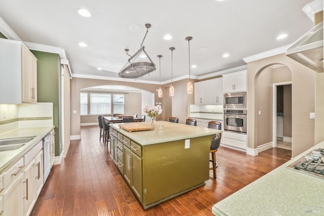 kitchen with arched walkways, white cabinets, dark wood finished floors, appliances with stainless steel finishes, and a kitchen bar