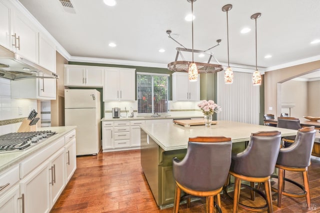 kitchen with arched walkways, under cabinet range hood, stainless steel gas stovetop, freestanding refrigerator, and crown molding