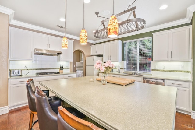 kitchen with arched walkways, crown molding, gas stovetop, freestanding refrigerator, and under cabinet range hood