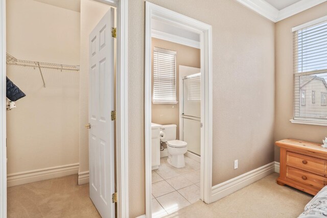 bedroom with light tile patterned floors, baseboards, connected bathroom, light colored carpet, and ornamental molding