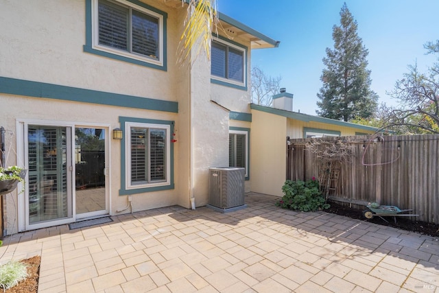 rear view of house featuring a patio, central AC, fence, stucco siding, and a chimney