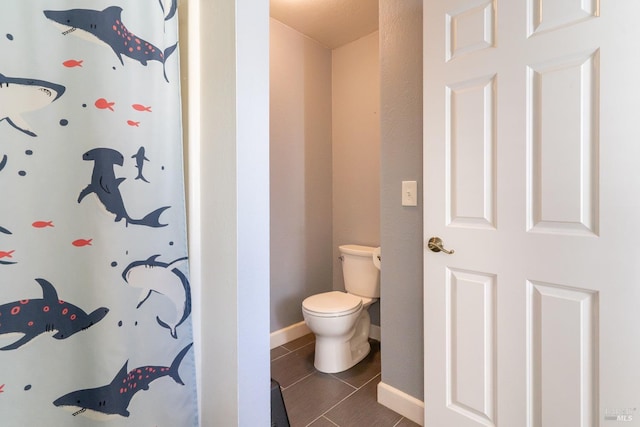 bathroom with a shower with shower curtain, tile patterned flooring, baseboards, and toilet