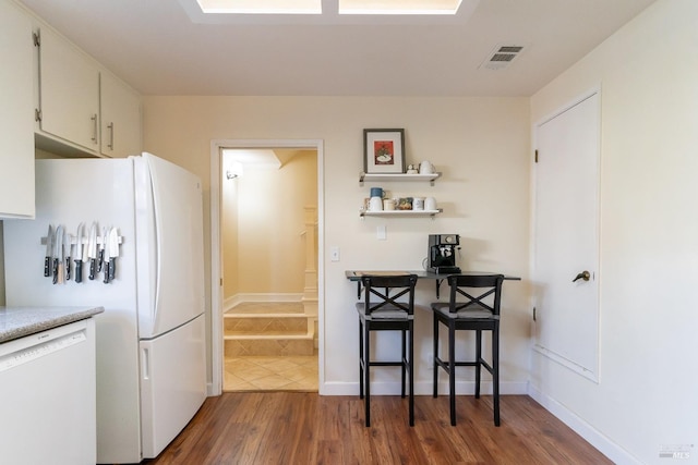 kitchen featuring white appliances, wood finished floors, visible vents, white cabinetry, and light countertops