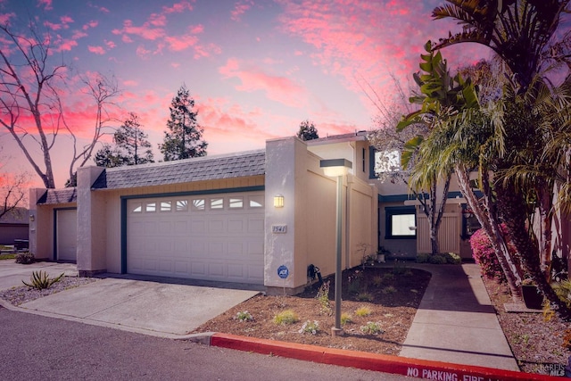 view of front of house featuring a garage, concrete driveway, a shingled roof, and stucco siding