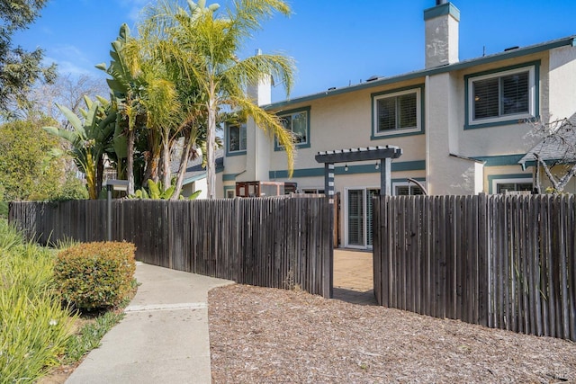 view of front of house with a fenced front yard, a chimney, a pergola, and stucco siding