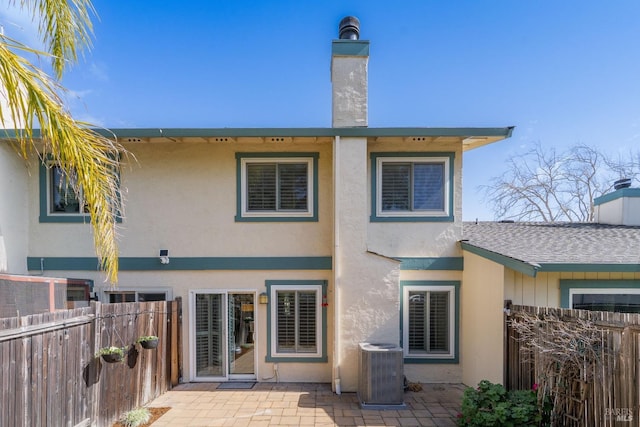 rear view of property with a chimney, stucco siding, a patio area, central AC, and fence