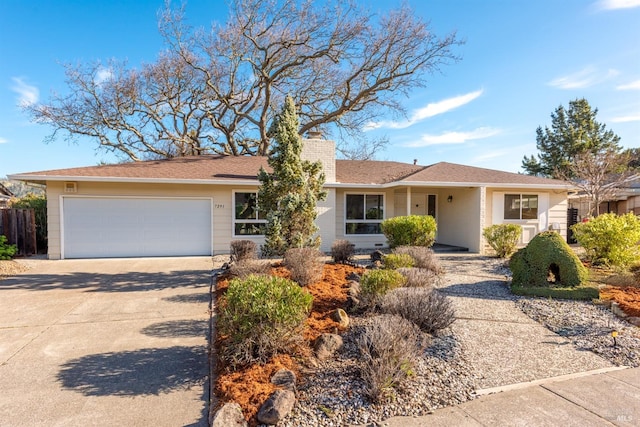 ranch-style home featuring concrete driveway, a chimney, an attached garage, and fence