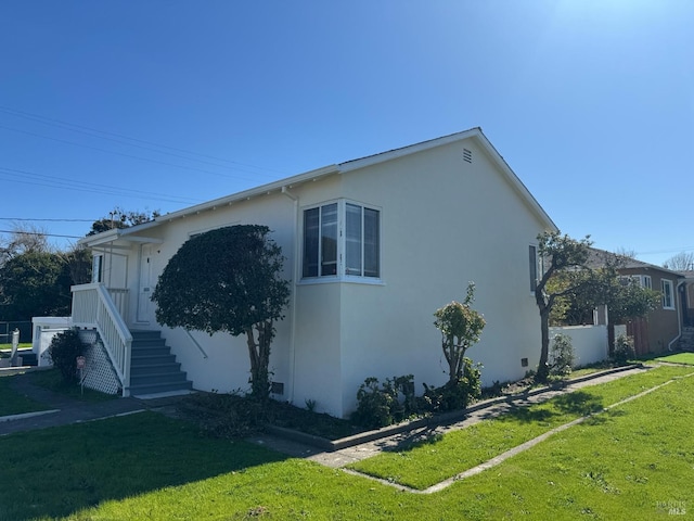 view of side of home featuring stucco siding, fence, and a yard