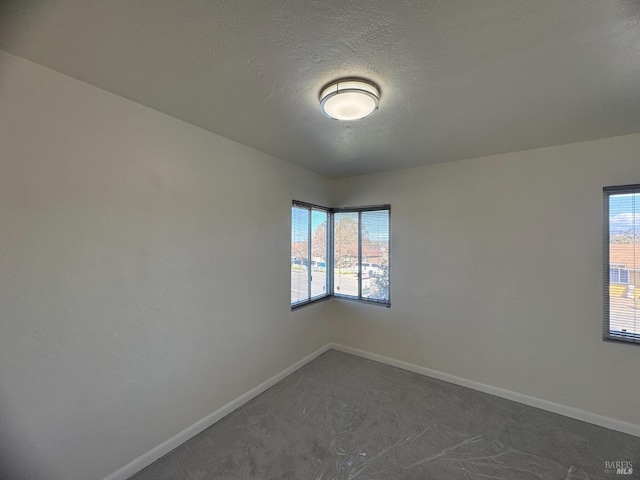 unfurnished room with baseboards, dark colored carpet, and a textured ceiling