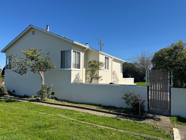 view of property exterior with a gate, fence, a lawn, and stucco siding