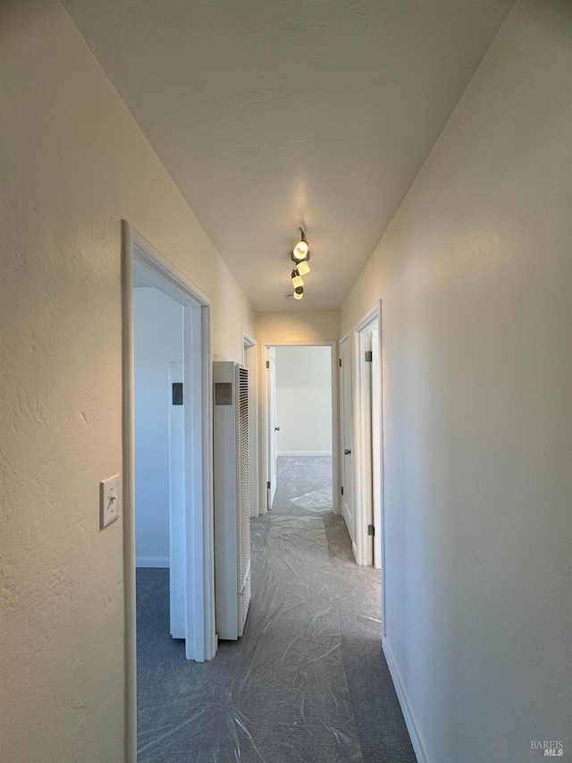 corridor with a textured wall, dark colored carpet, and baseboards