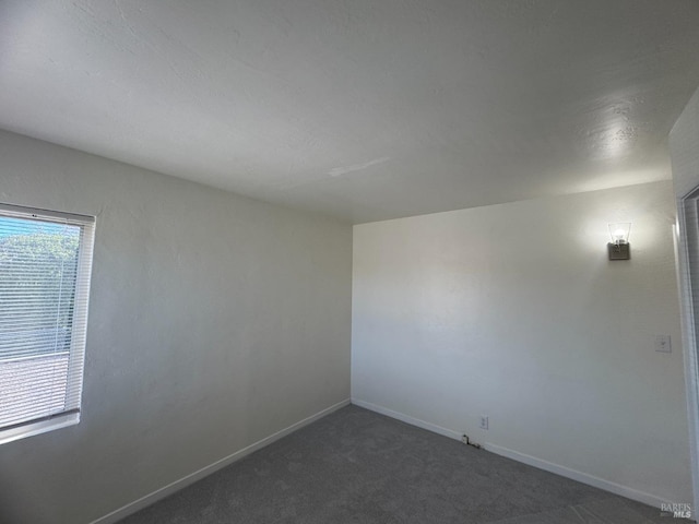 empty room featuring baseboards and dark colored carpet