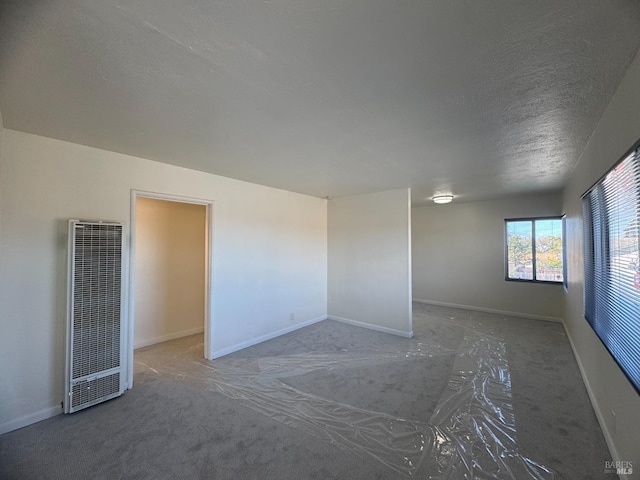 unfurnished room with a heating unit, a textured ceiling, and baseboards