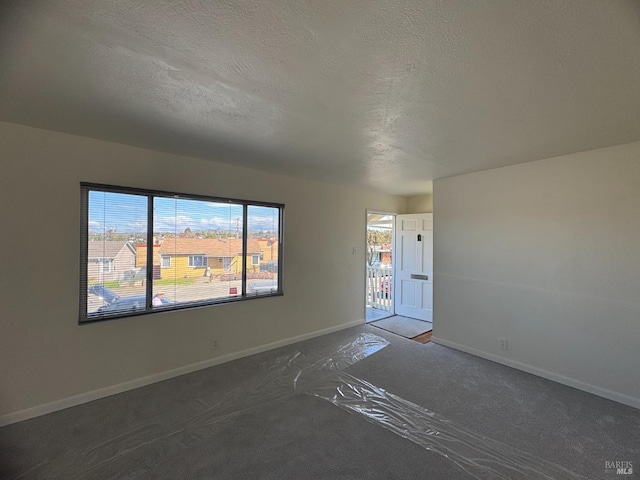 carpeted empty room featuring a textured ceiling and baseboards