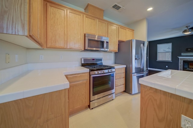 kitchen featuring visible vents, tile counters, ceiling fan, appliances with stainless steel finishes, and light brown cabinetry