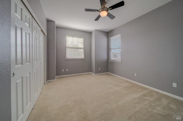 unfurnished bedroom featuring a closet, baseboards, a ceiling fan, and light colored carpet