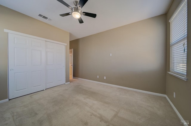 unfurnished bedroom featuring light colored carpet, a ceiling fan, baseboards, visible vents, and a closet