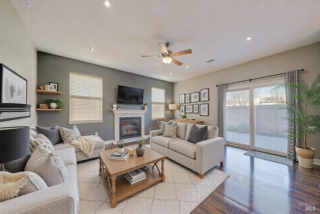 living room featuring baseboards, a ceiling fan, a glass covered fireplace, wood finished floors, and recessed lighting