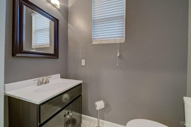 bathroom with baseboards, a textured wall, vanity, and toilet