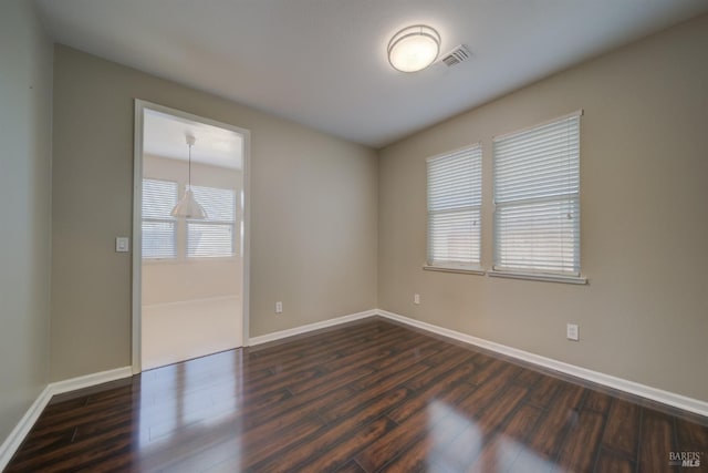 unfurnished room with dark wood-style flooring, visible vents, and baseboards